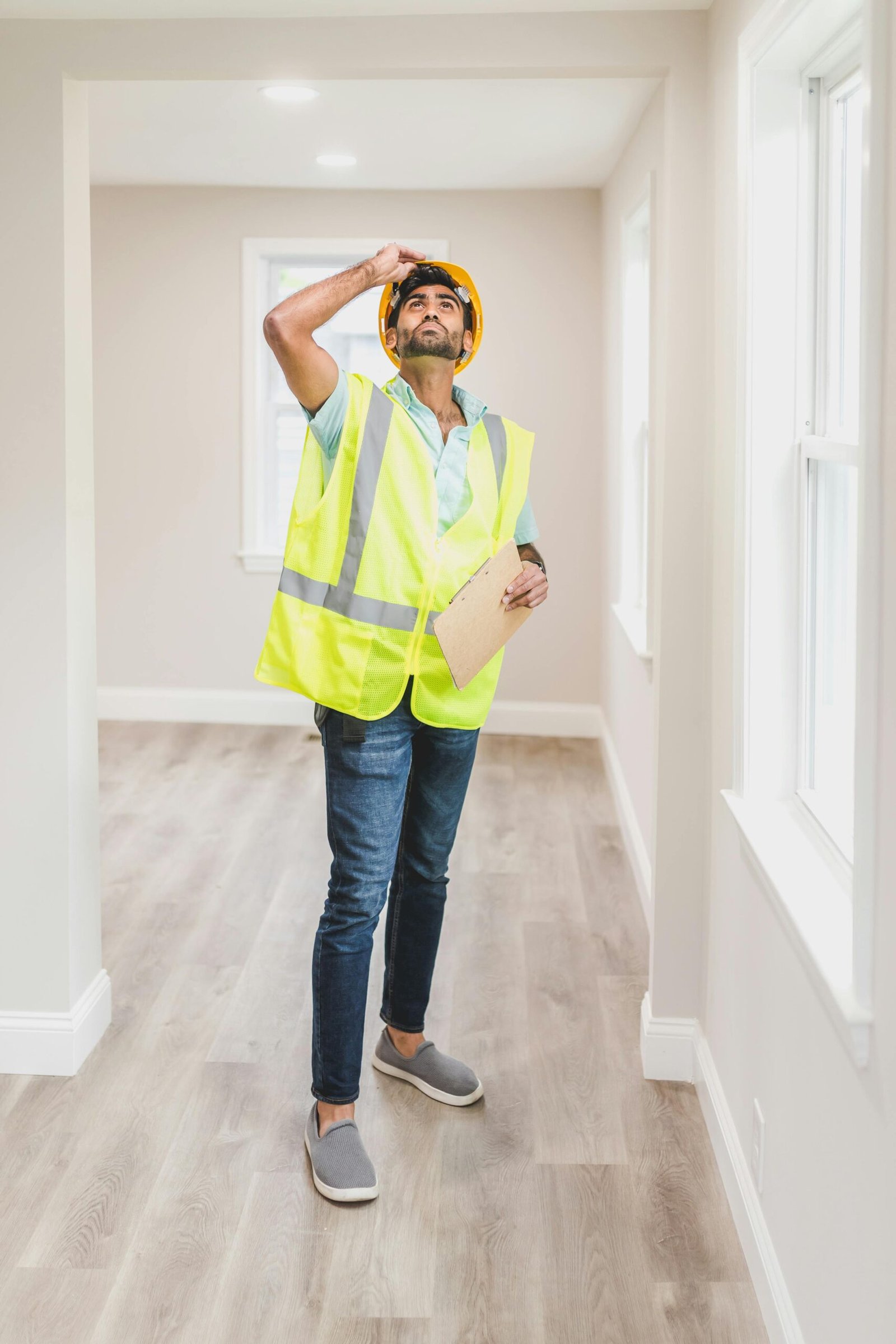 Construction inspector in a safety vest and hard hat examining an empty house interior.